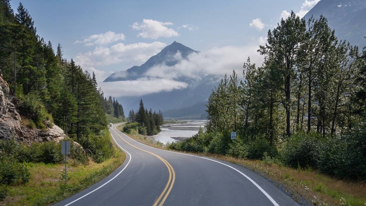 Winding road through Alaksan country side, surrounded by mountains, a small lake, and evergreen trees